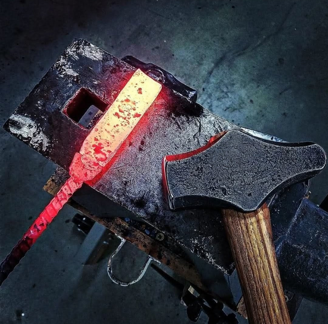 Red hot steel on an anvil next to a blacksmith hammer.